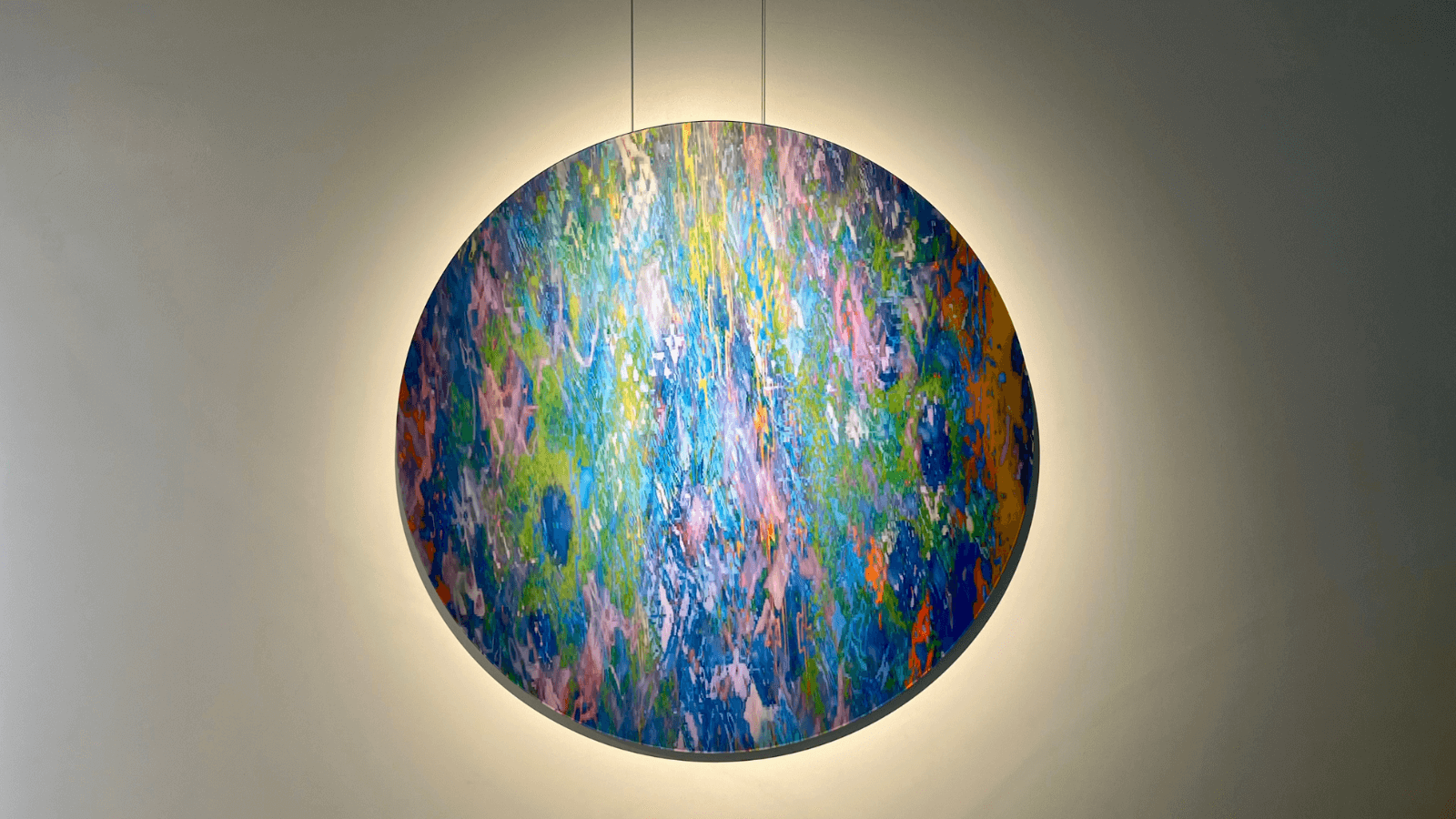Vibrant conceptual art painting in circular frame, featuring a blend of colors and textures, illuminated against a gray wall.