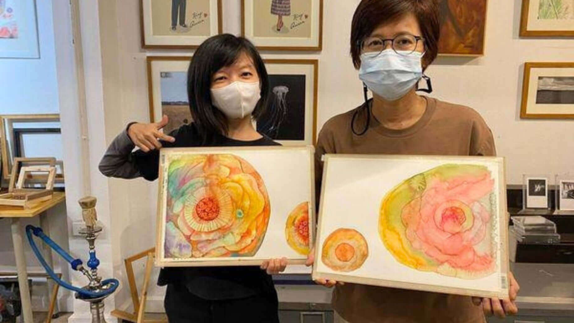 Two people holding colourful watercolour paintings at Supmanee’s Watercolour Workshop, both wearing masks and smiling.