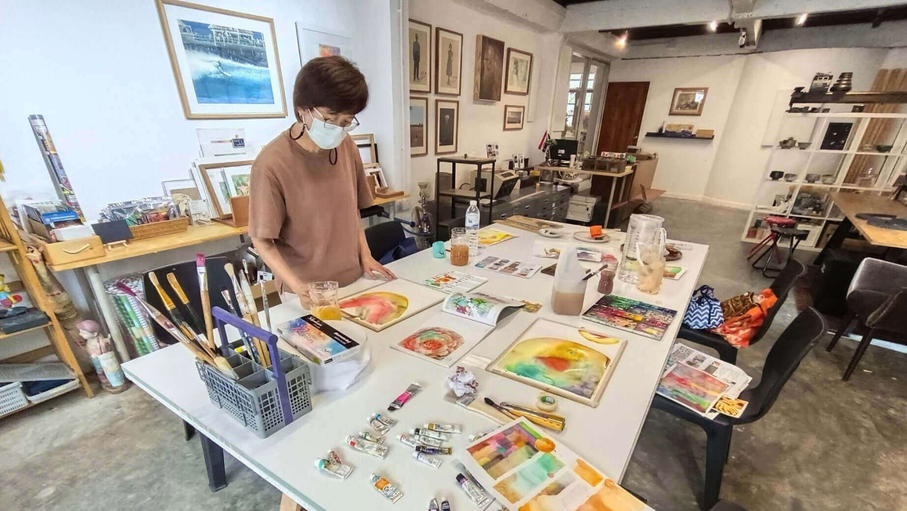 Artist in a watercolour workshop painting artworks on a table filled with art supplies in a studio.