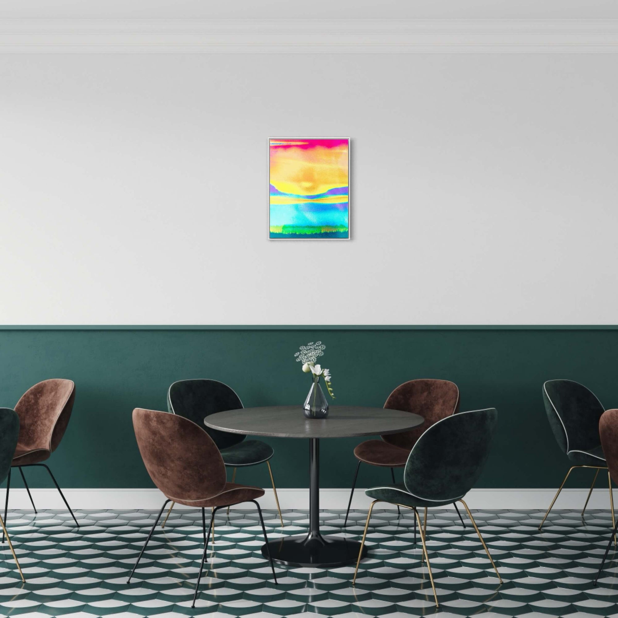 The image shows a dining area with a circular table surrounded by velvet chairs in a room with a two-tone wall. The bottom half is dark green and the top half is white. Above the table, against the white part of the wall, hangs "Raising Energy I," a bright, colourful artwork with hues of yellow, blue, and a dash of pink. The artwork adds a splash of colour and energy to the sophisticated, muted tones of the room.