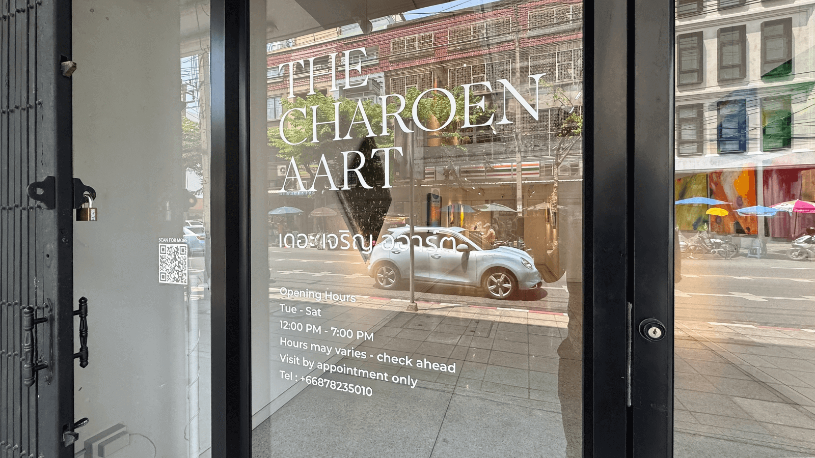The exterior of The Charoen Aart with visible hours and contact details on glass door.