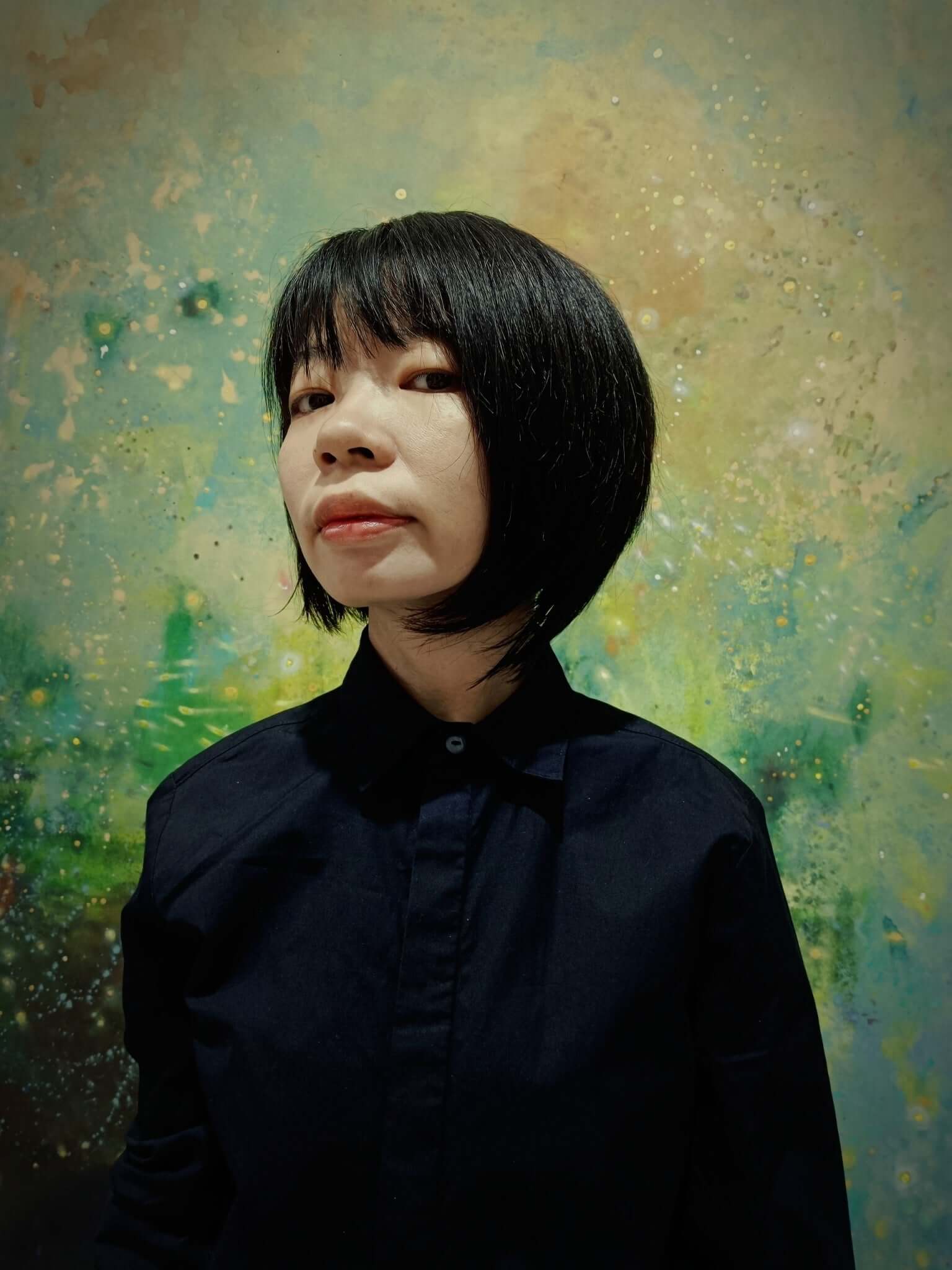 Woman in a black shirt with short dark hair against an abstract, colourful background