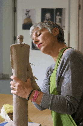 Christine Blom sculpting a clay figure with focus and care in a studio.