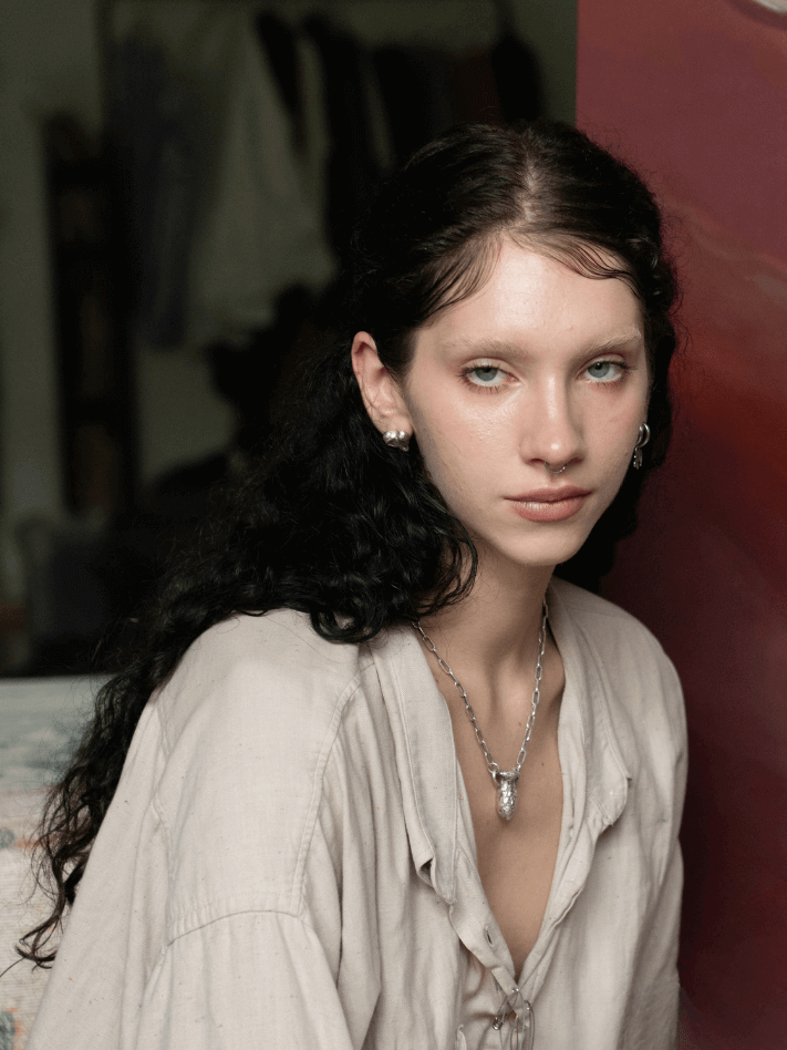 Yasy Bachurina, with long black hair wearing a beige blouse, sitting indoors with a serious expression.