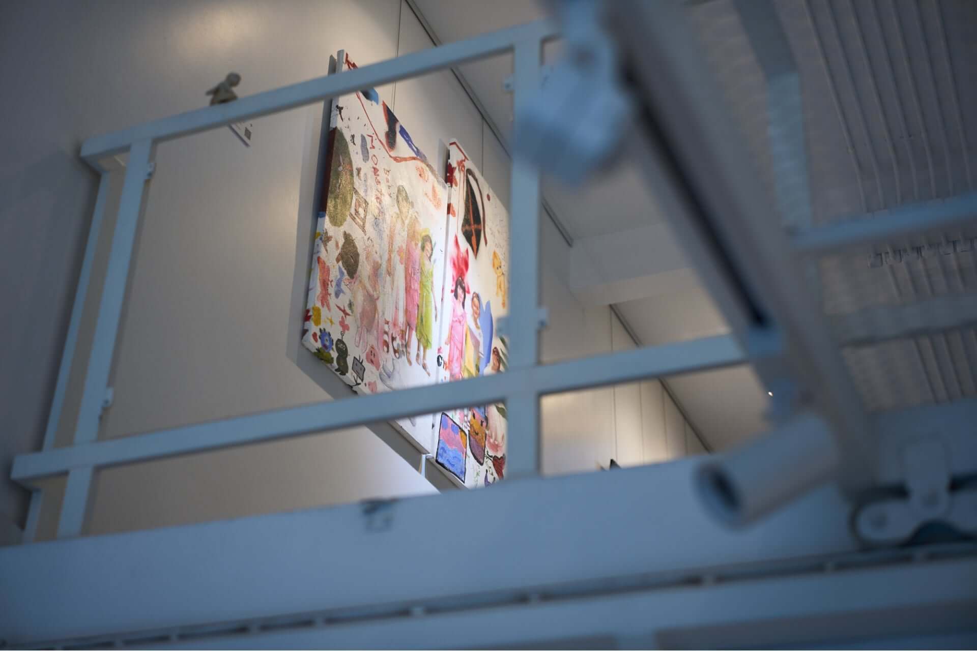 Art display on a wall viewed through an industrial-style railing with a focus on vibrant colors and creative design elements.