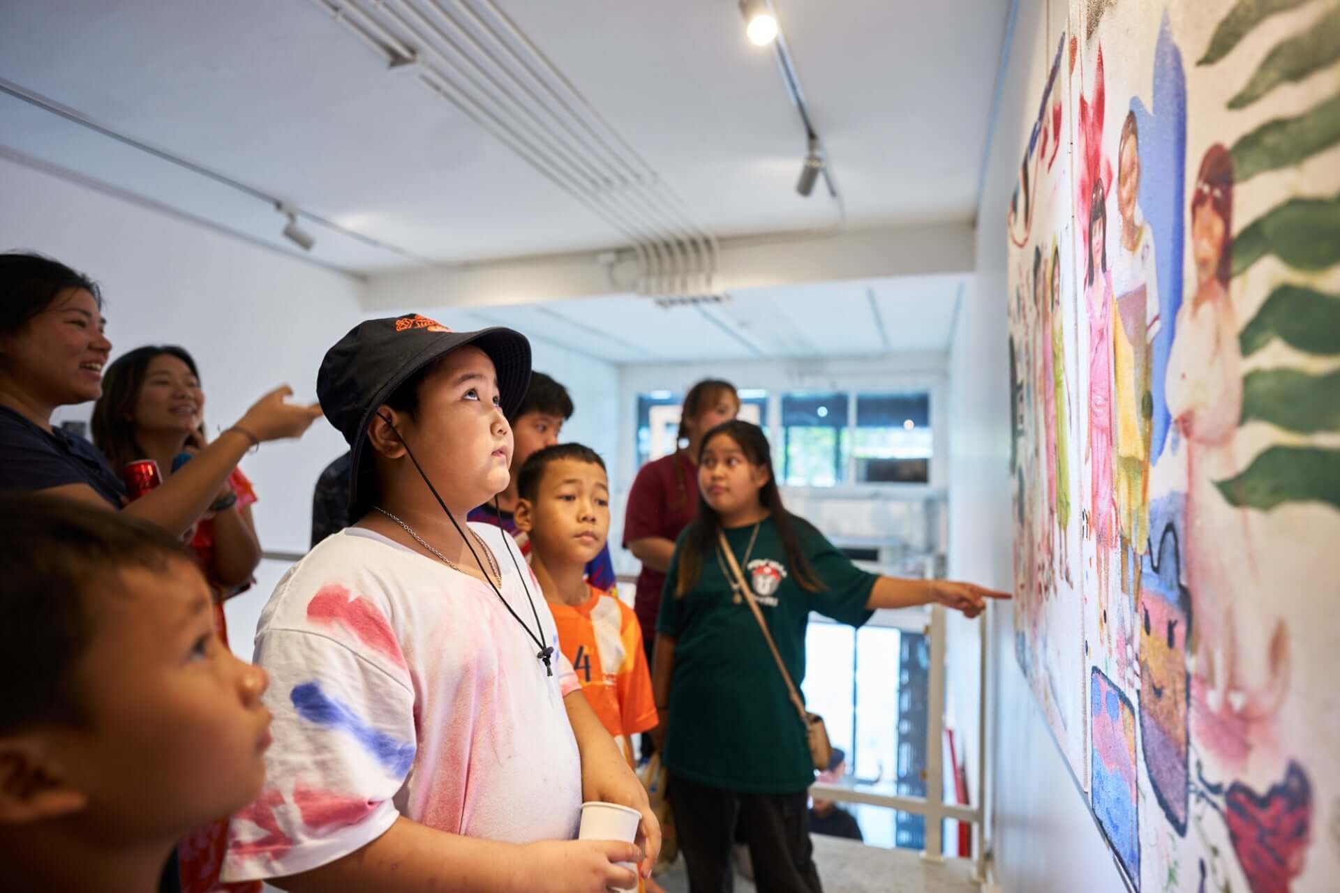 Group of children observing artwork in a gallery setting, engaged and curious about the colorful mural on display.