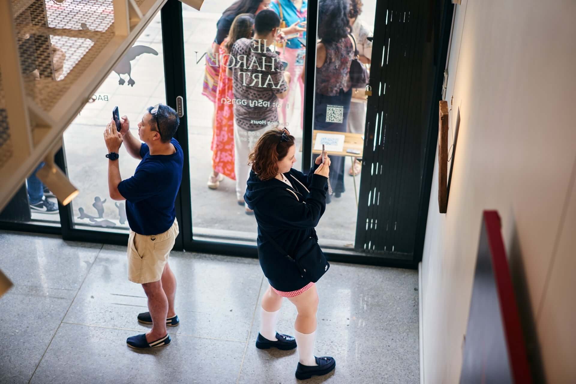 Visitors capturing art in gallery with smartphones near entrance.