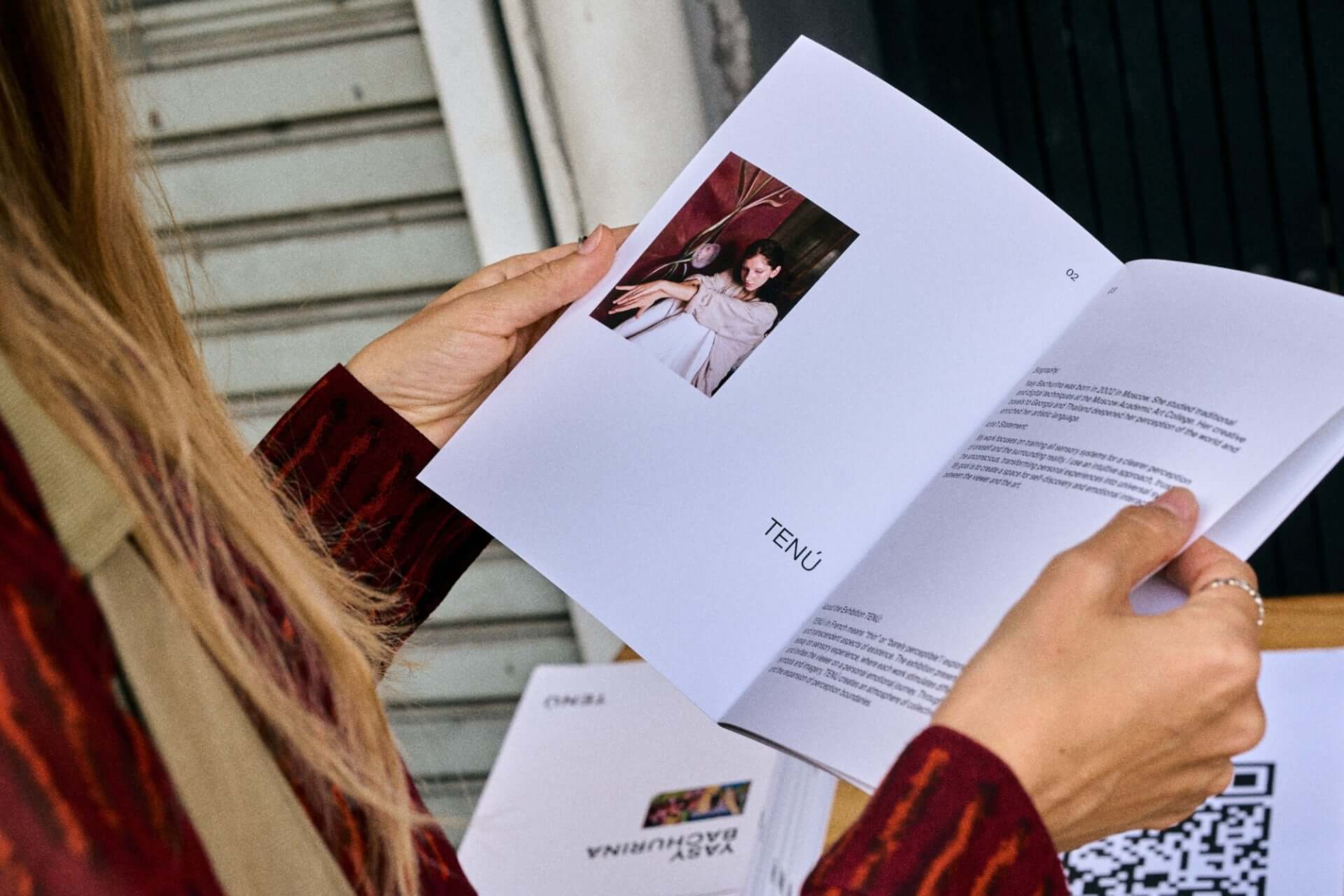 Person reading a booklet with a fashion model photo and text, wearing a red patterned jacket.