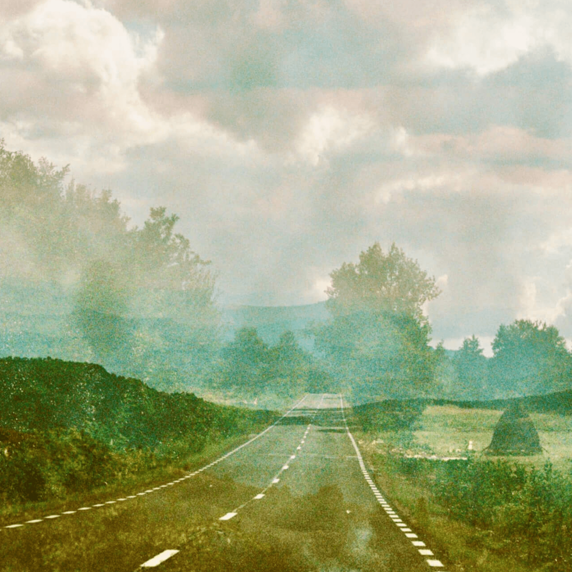 Scenic view of a winding road through lush greenery under a cloudy sky, creating a dreamy atmosphere.