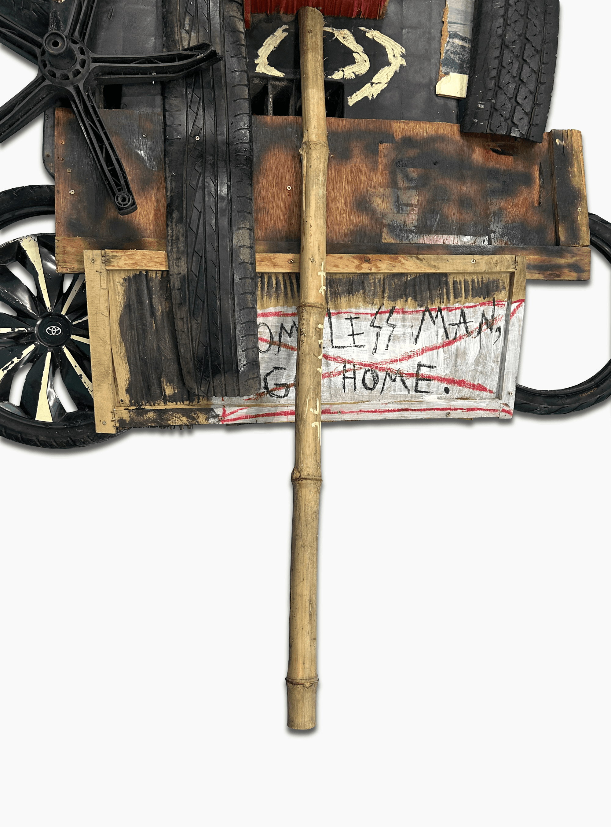 A collection of discarded materials including tires, wood, and a bamboo stick, arranged with a message about homelessness.