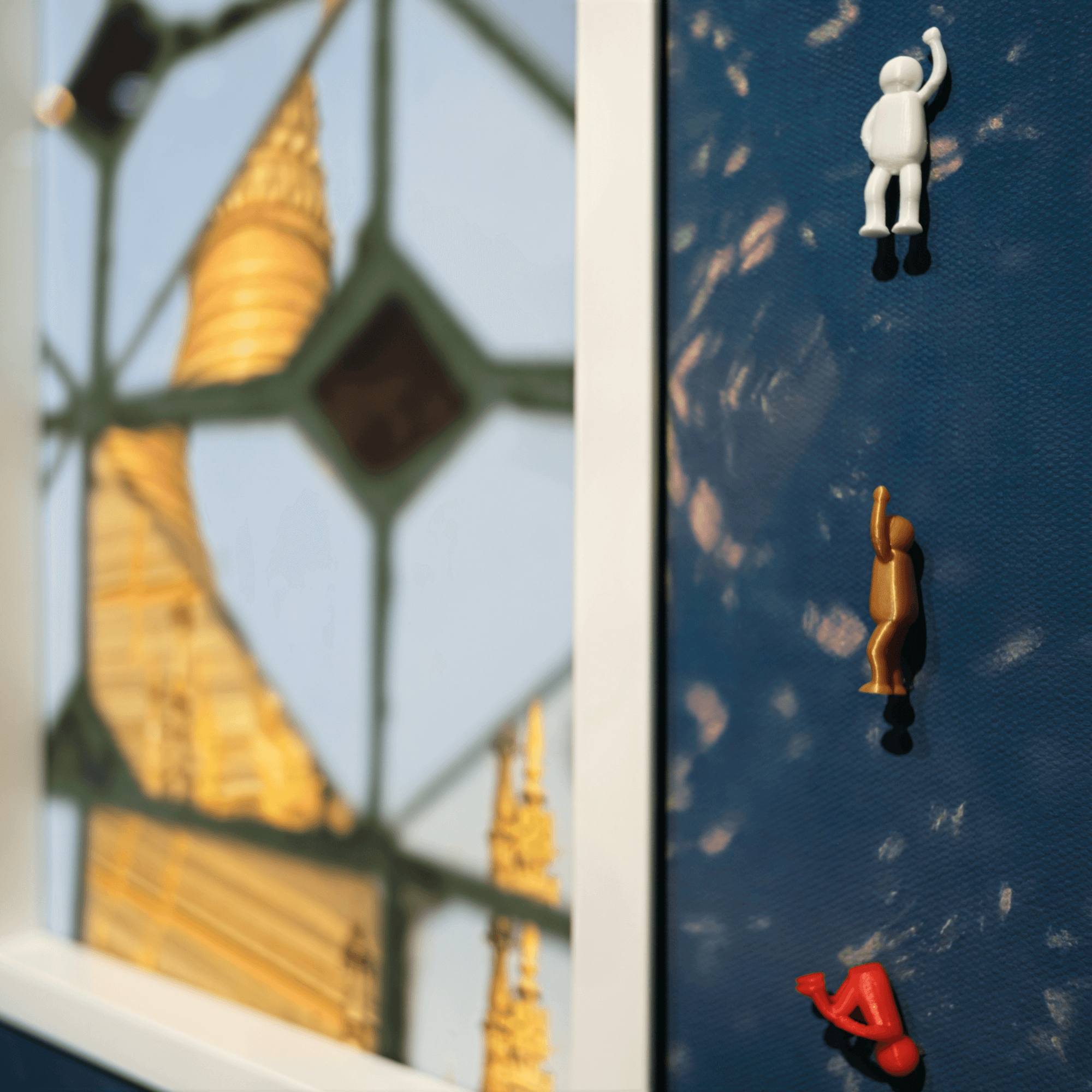 Image featuring miniature figures on a blue surface with a background of a golden spire, representing Continous Line, 2025.