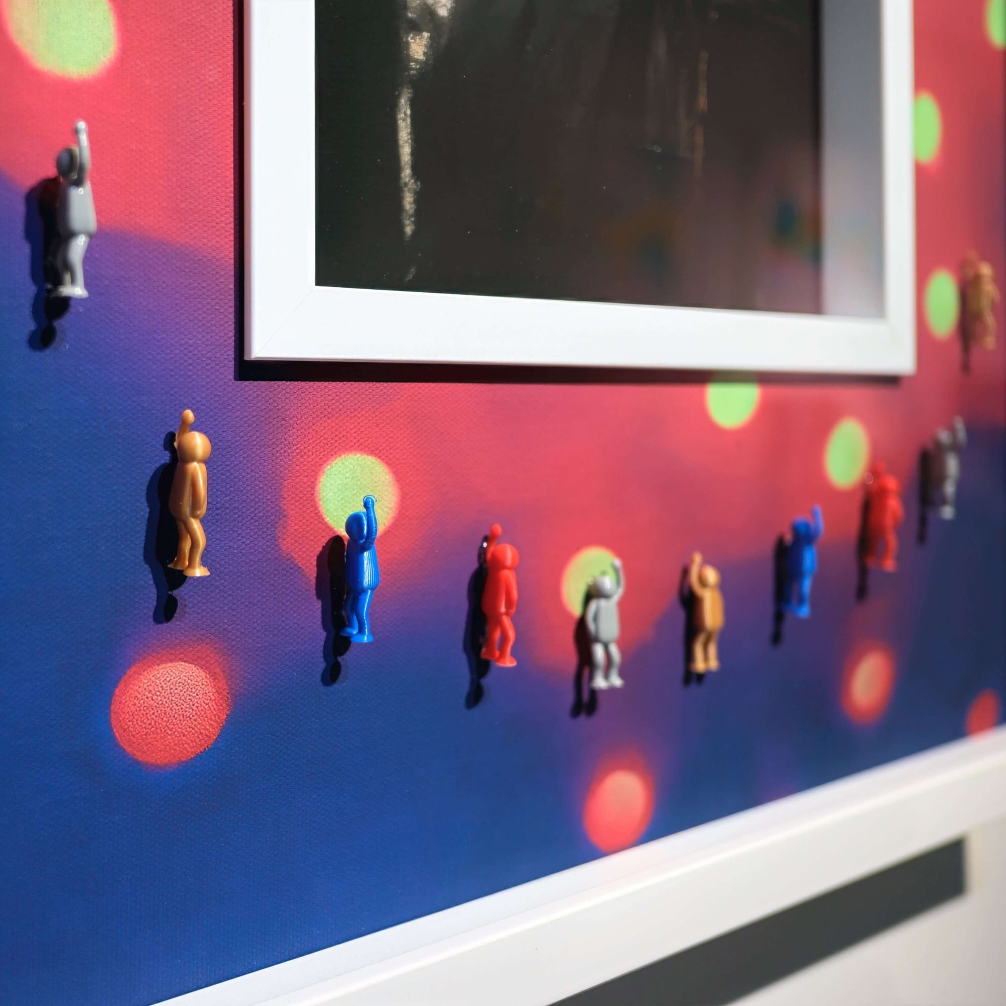 Colorful miniature figures on a vibrant wall art, featuring bright bokeh lights and a framed photo.
