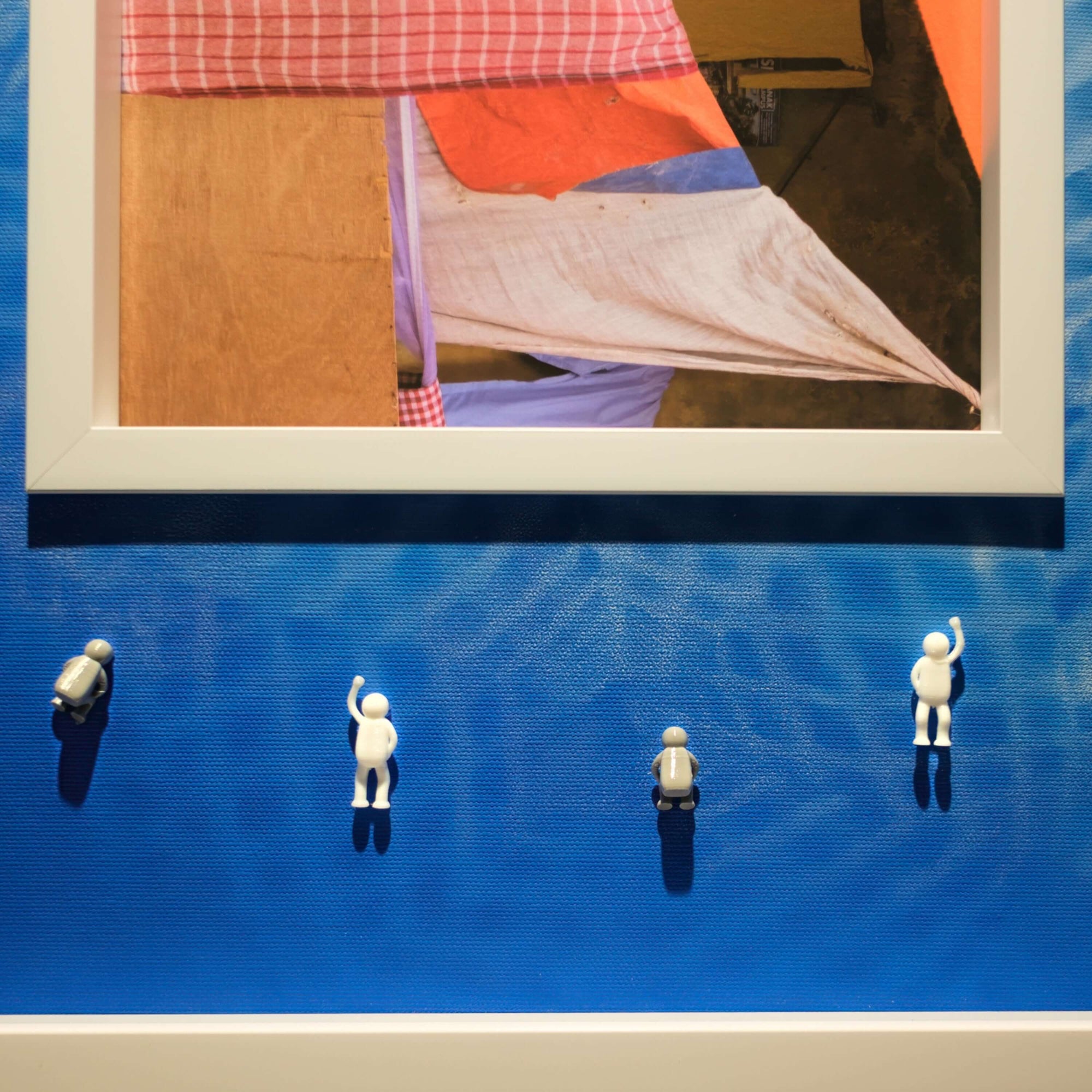 Covered Memory, 2025 art installation featuring small figurines on a blue wall with a colorful framed artwork.