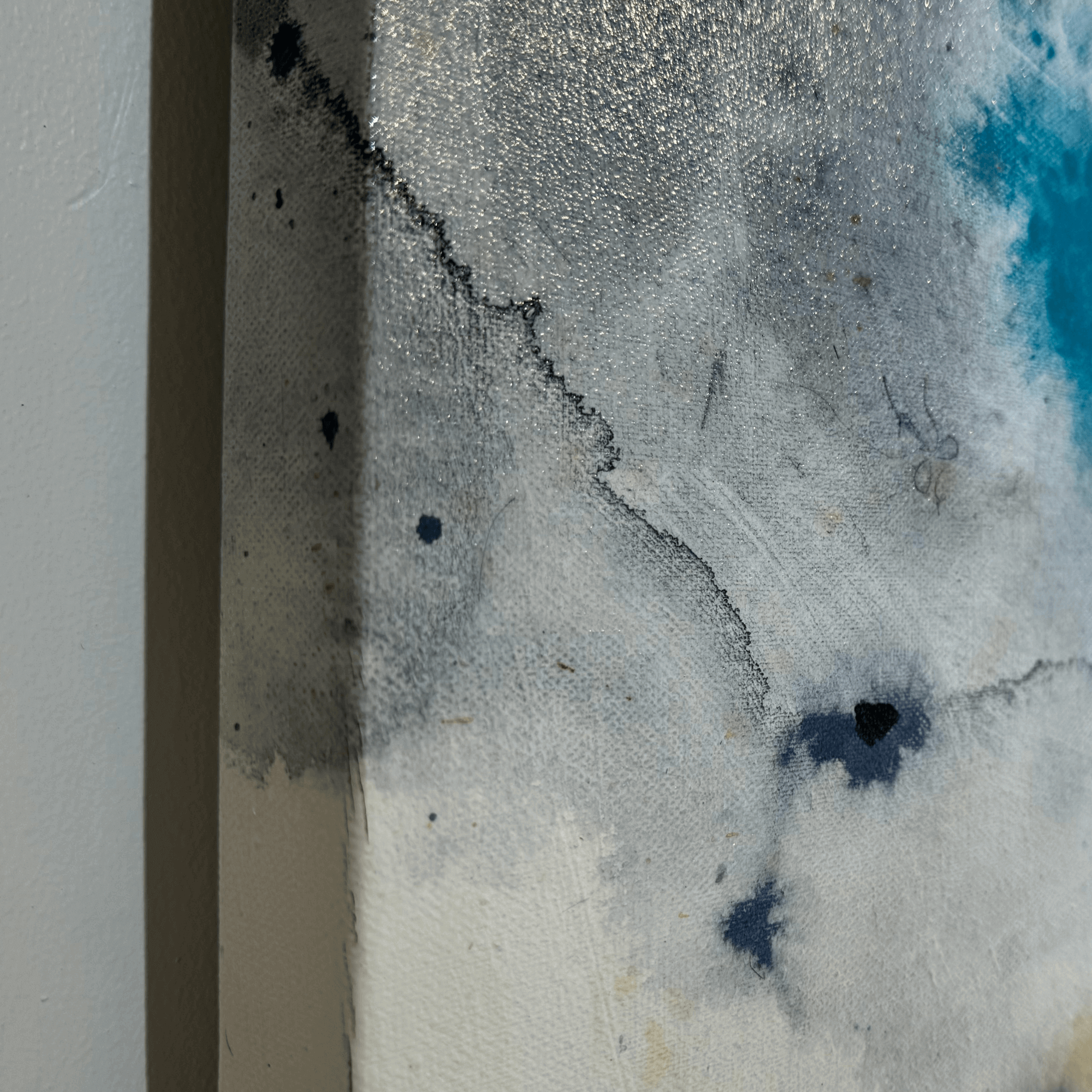 Close-up of texture and edges on an unframed abstract acrylic painting on canvas showing shades of blue and grey with a smooth, textured surface.