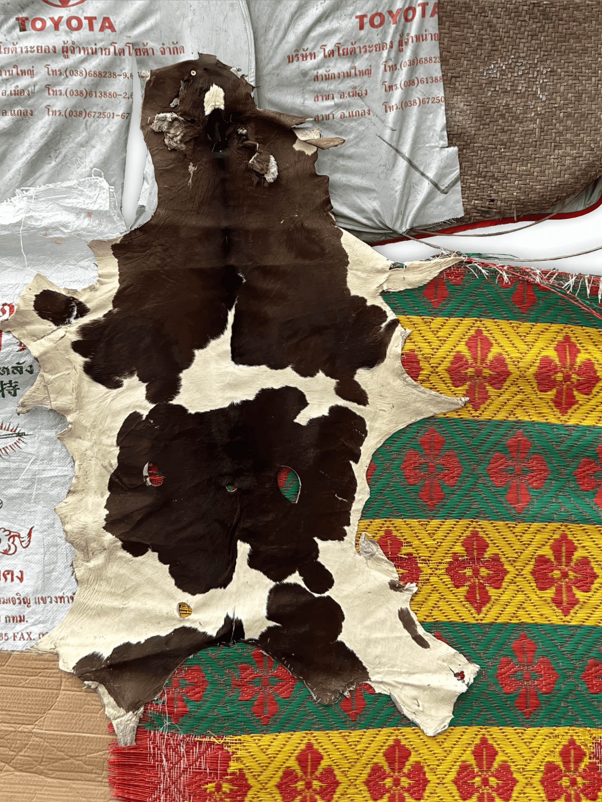Cowhide rug with brown and white patterns, laid over colorful woven fabrics.