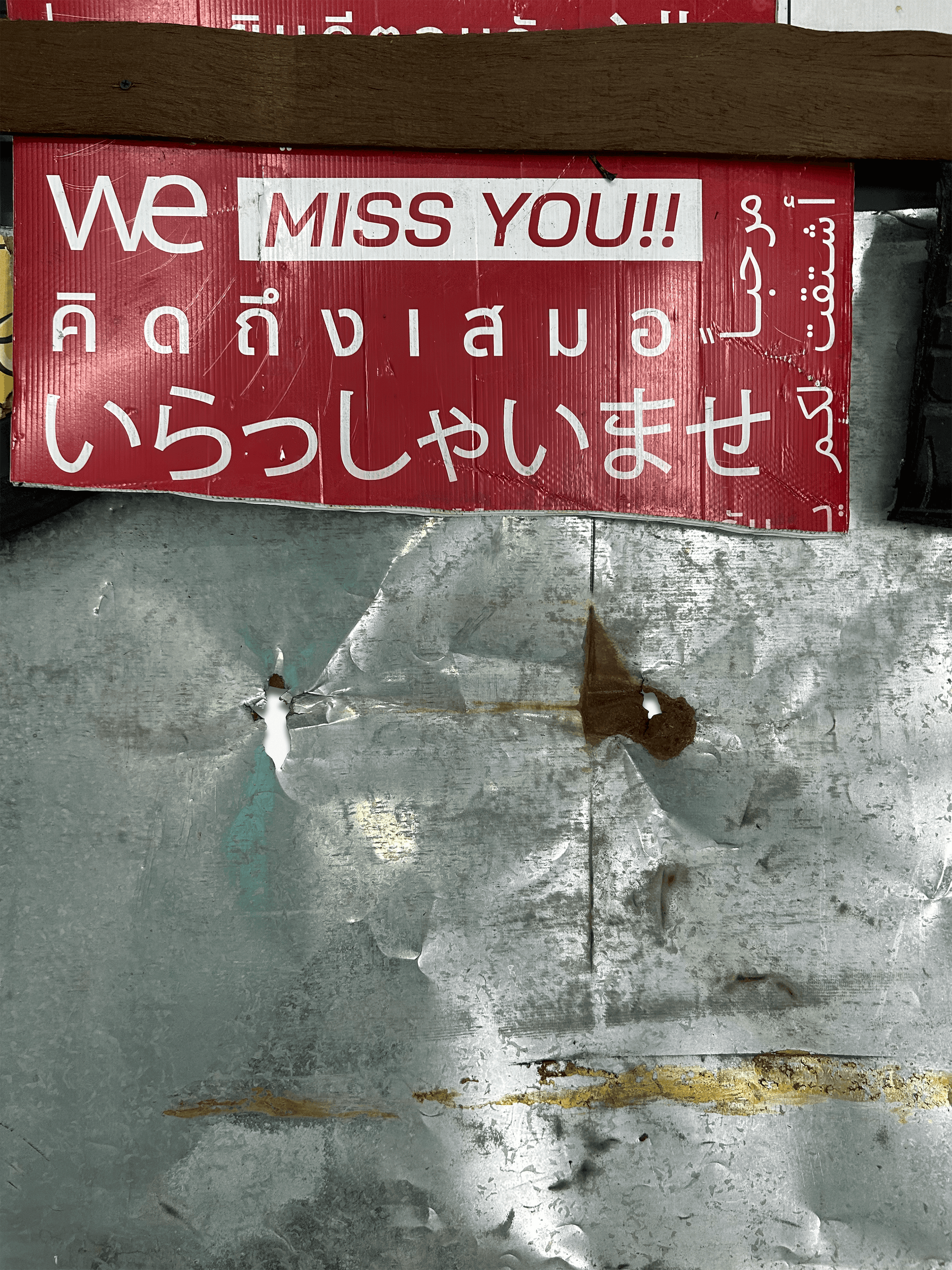 A colorful sign displaying 'We miss you!!' in English and other languages on a weathered metallic background.